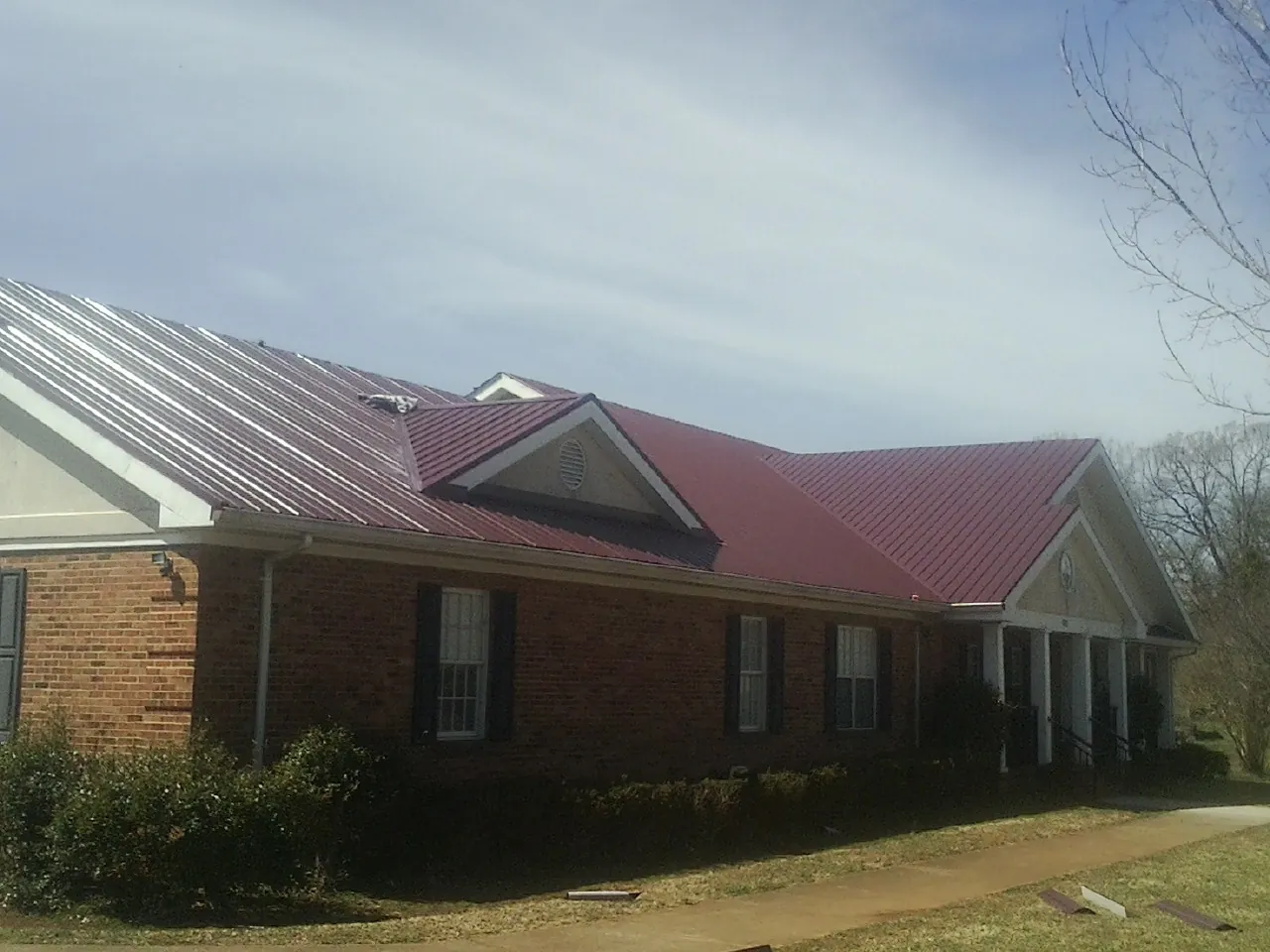 Red metal roof with gabled entries on a long brick building, from a Hail Damage Roof Repair job in Point Reyes Station
