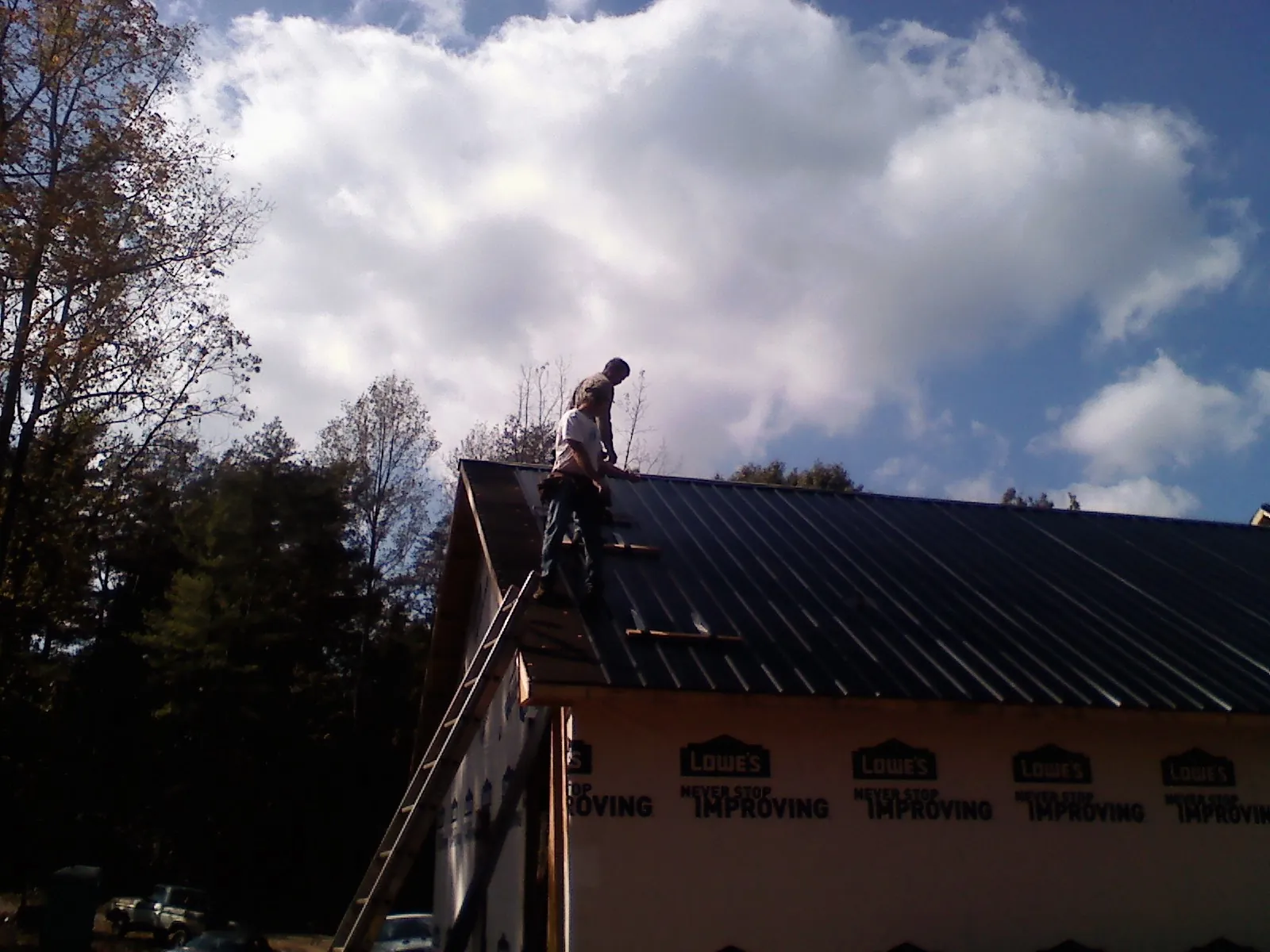 Roofer fastening dark metal panels high against a cloudy sky, from a Roof Inspection job in Point Reyes Station