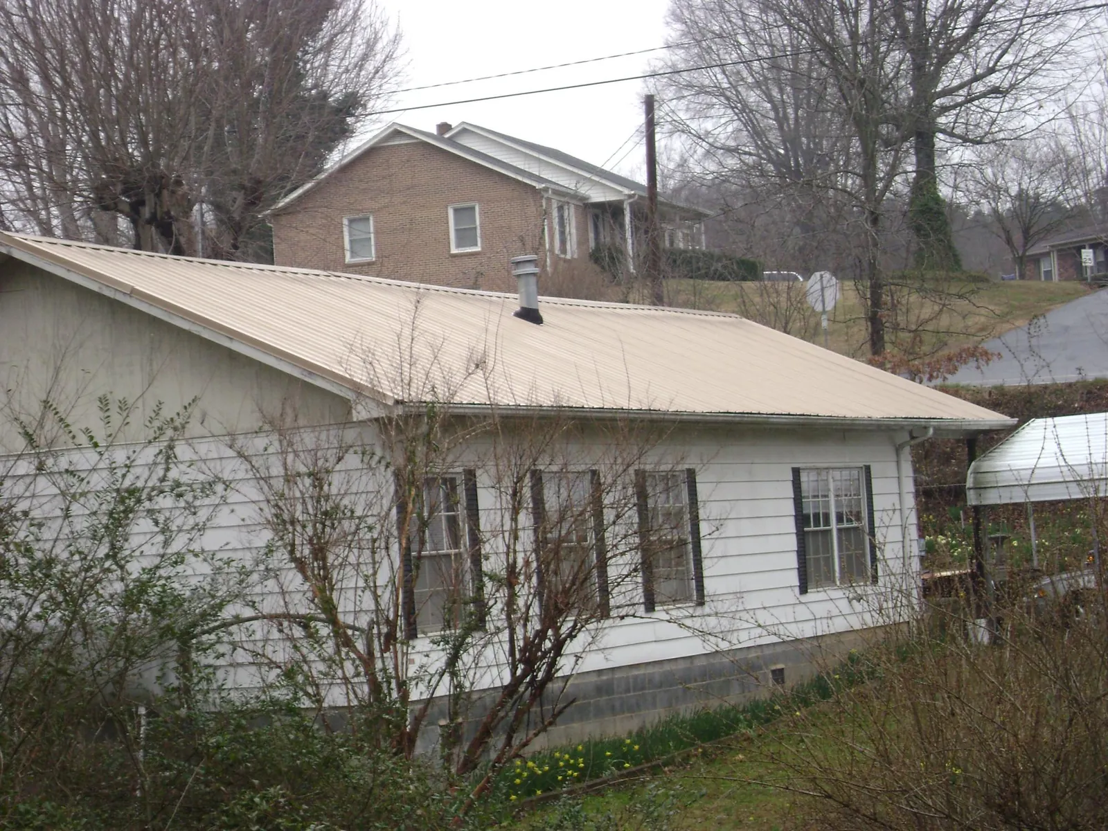 Tan metal roof on a white sided house set into a hillside — Commercial Roofing by Roofing Brothers in Point Reyes Station